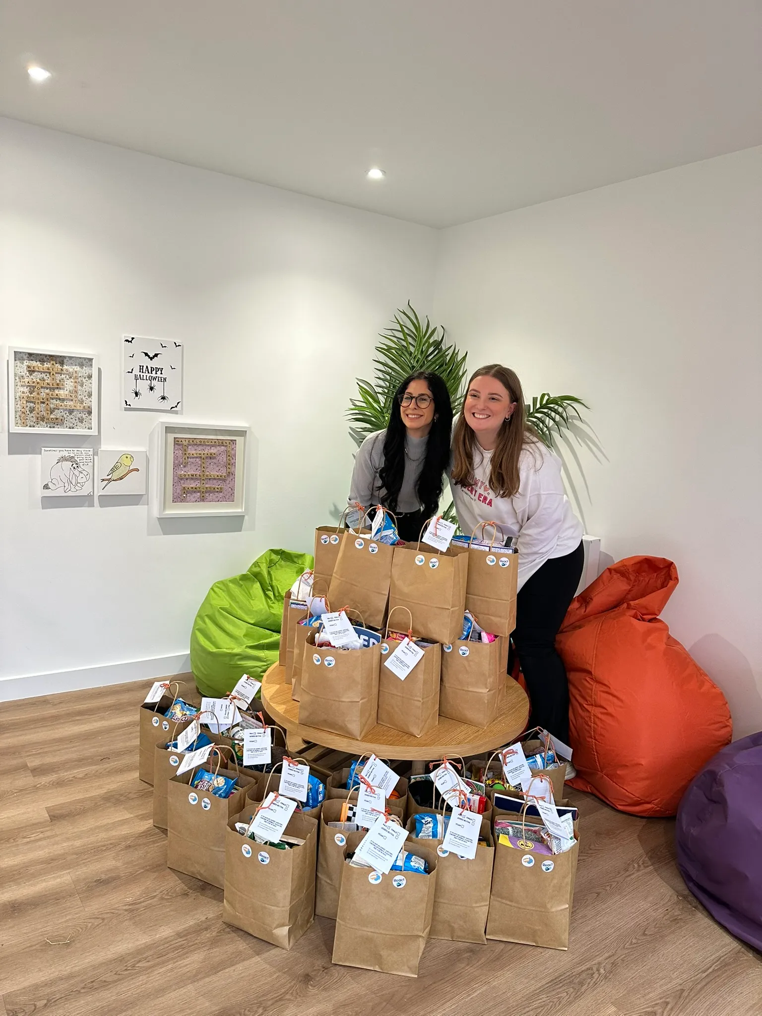 Two Hope Bags volunteers standing behind a table piled high with packed Hope Bags ready for delivery