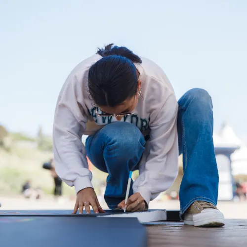 A volunteer crouching down to handwrite a message of hope on a sign at an outdoor pop-up